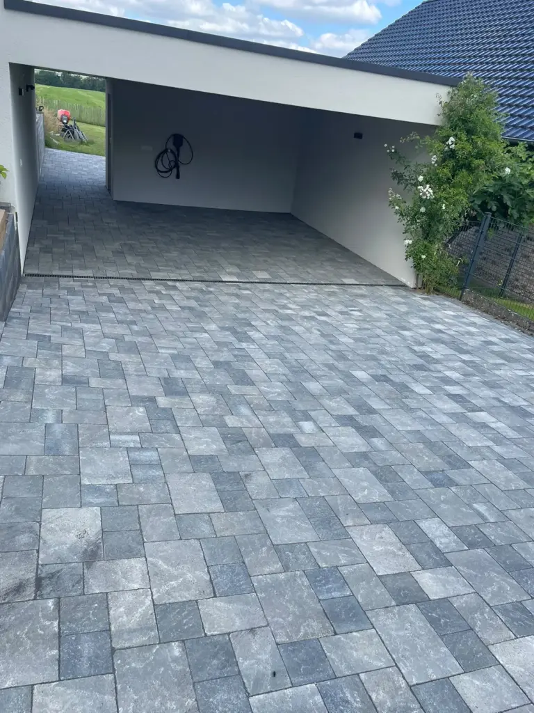 Neu gepflasterte Einfahrt mit grauem Pflaster vor einem Carport