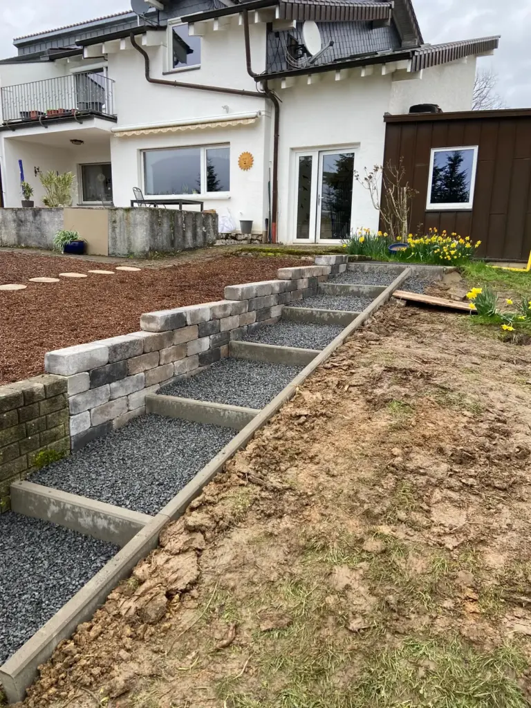Gartentreppe mit Schotterstufen und Einfassung im Hanggarten, daneben eine Mauer aus Blocksteinen