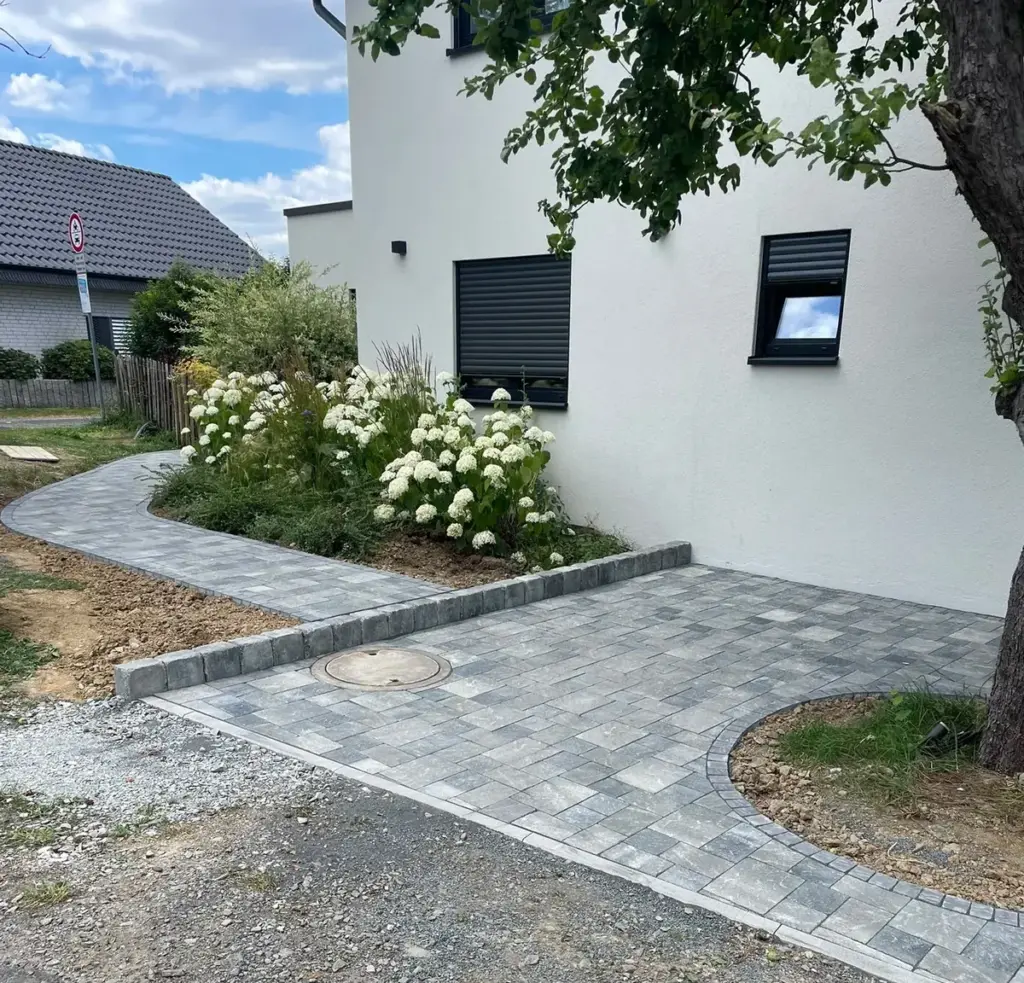 Gepflasterter Weg mit Einfassung entlang eines Hauses, daneben ein Beet mit Hortensien