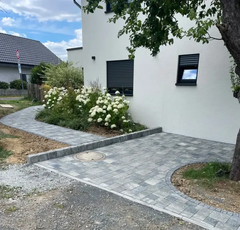 Gepflasterter Weg mit Einfassung entlang eines Hauses, daneben ein Beet mit Hortensien