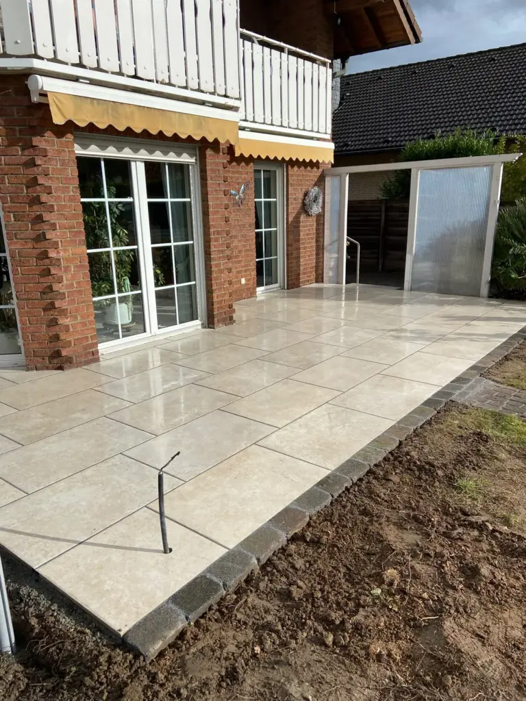 Neue Terrasse aus hellen Großformat-Platten mit Randeinfassung vor einem Klinkerhaus