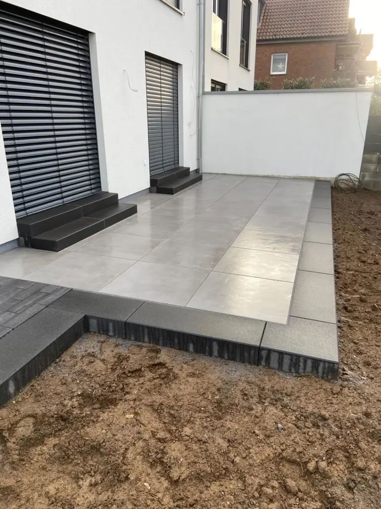 Terrasse aus großformatigen Platten mit Stufen vor bodentiefen Fenstern