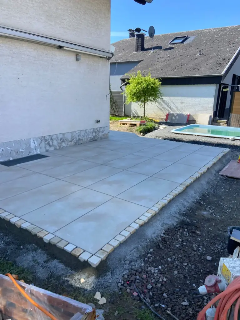 Terrasse aus großen hellen Platten mit Einfassung aus hellen Pflastersteinen