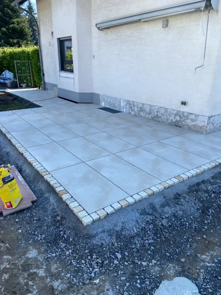 Helle Terrassenplatten mit Randeinfassung aus Pflastersteinen am Haus